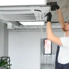 Instalator w kasku montuje klimatyzator kasetonowy na suficie.